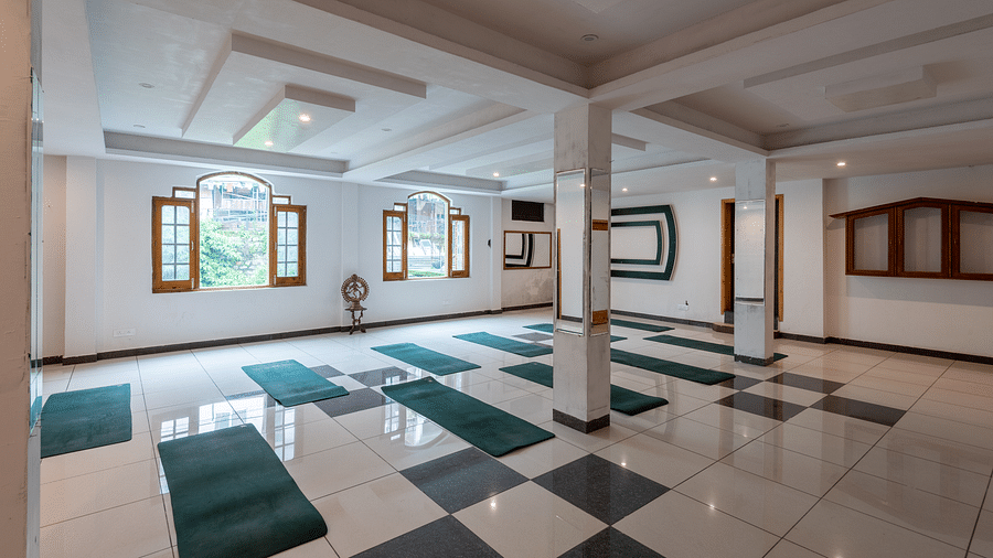 A spacious yoga studio with a tiled floor, large windows, and multiple green yoga mats laid out - DLS Meghavan Resort